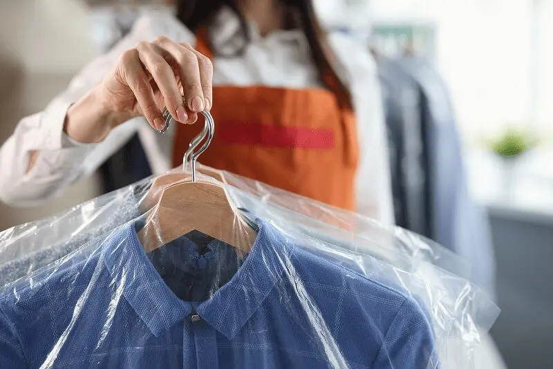 Person holding dry-cleaned shirt on hanger.