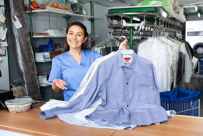 Woman holding freshly laundered shirts, smiling.